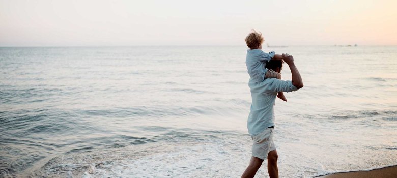 Father with a toddler boy walking on beach on summer holiday, having fun. Father with daughter on his arms