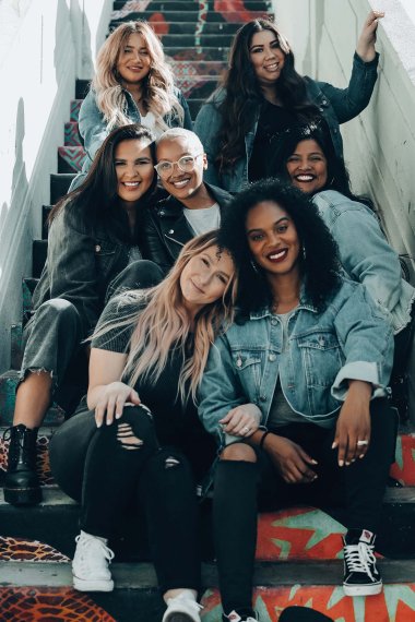 Eine Gruppe Frauen unterschiedlicher ethnischer Herkunft sitzen auf einer Treppe und lachen.