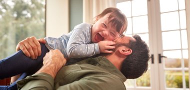 Loving Father Playing With Laughing Down Syndrome Daughter At Home Together Loving Father Playing With Laughing Down Syndrome Daughter At Home Together