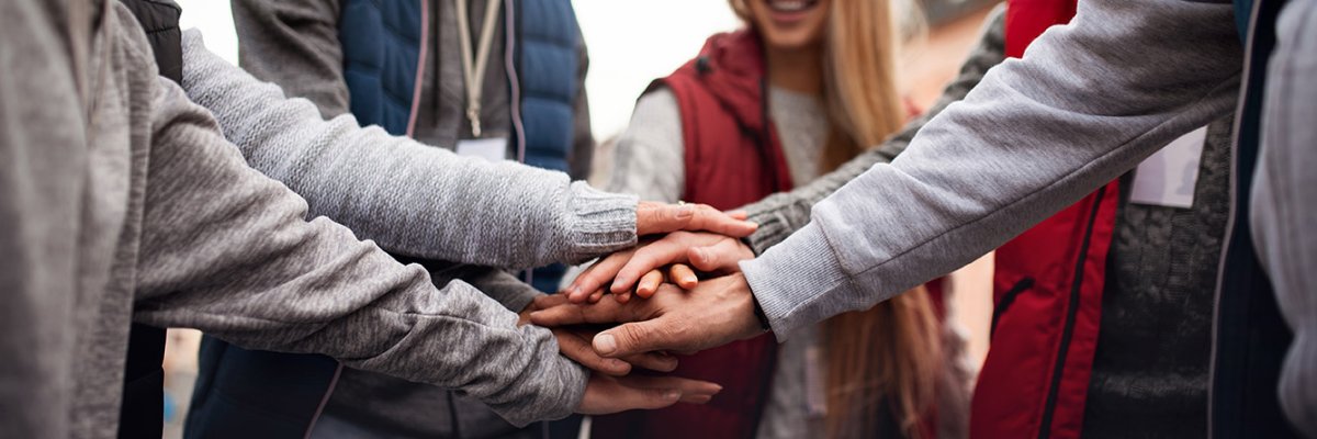 Close up of group of happy community service volunteers stacking hands together outdoors in street