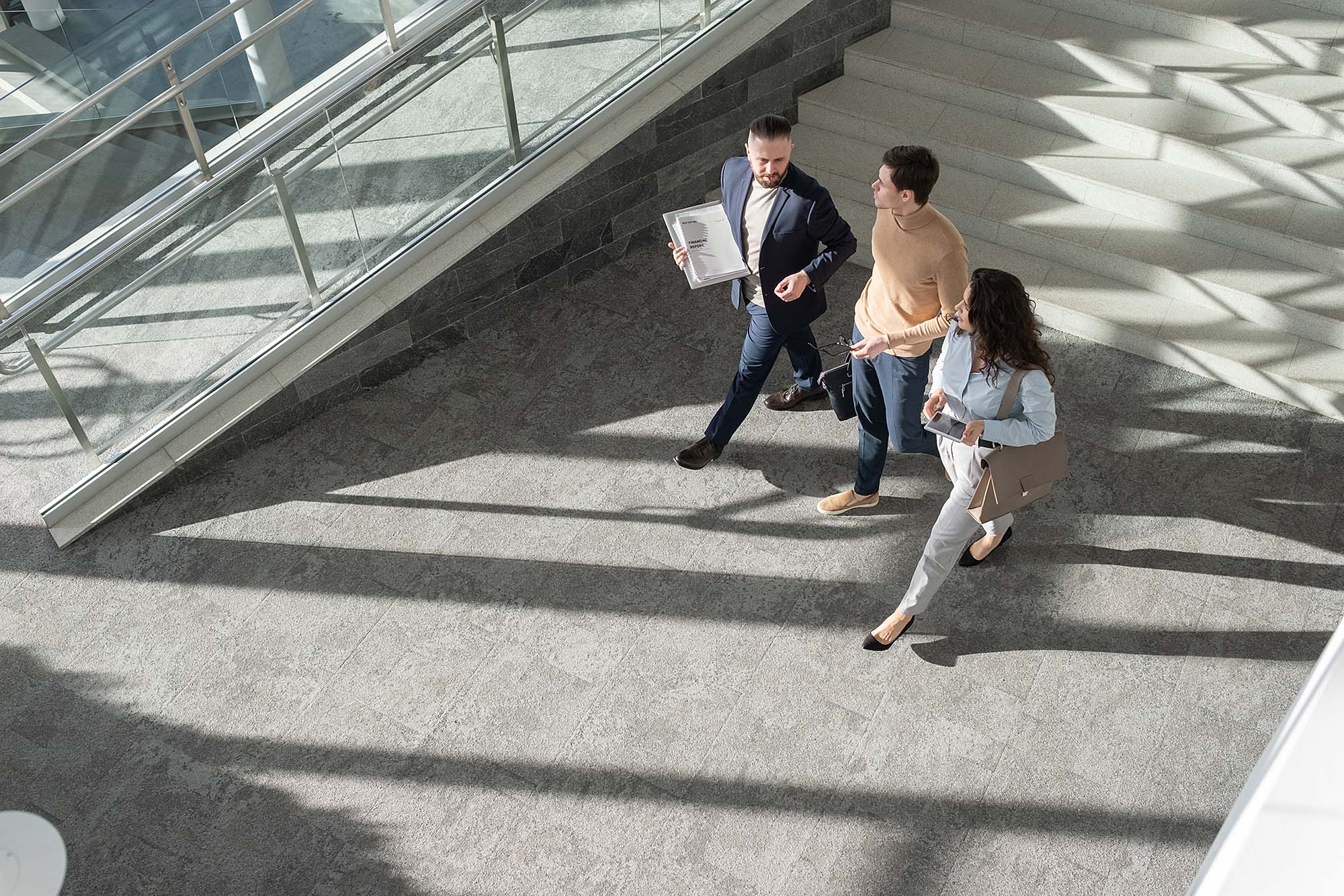 Above view of three young coworkers in formalwear moving down lounge of office center and discussing points of new business project