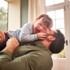 Loving Father Playing With Laughing Down Syndrome Daughter At Home Together