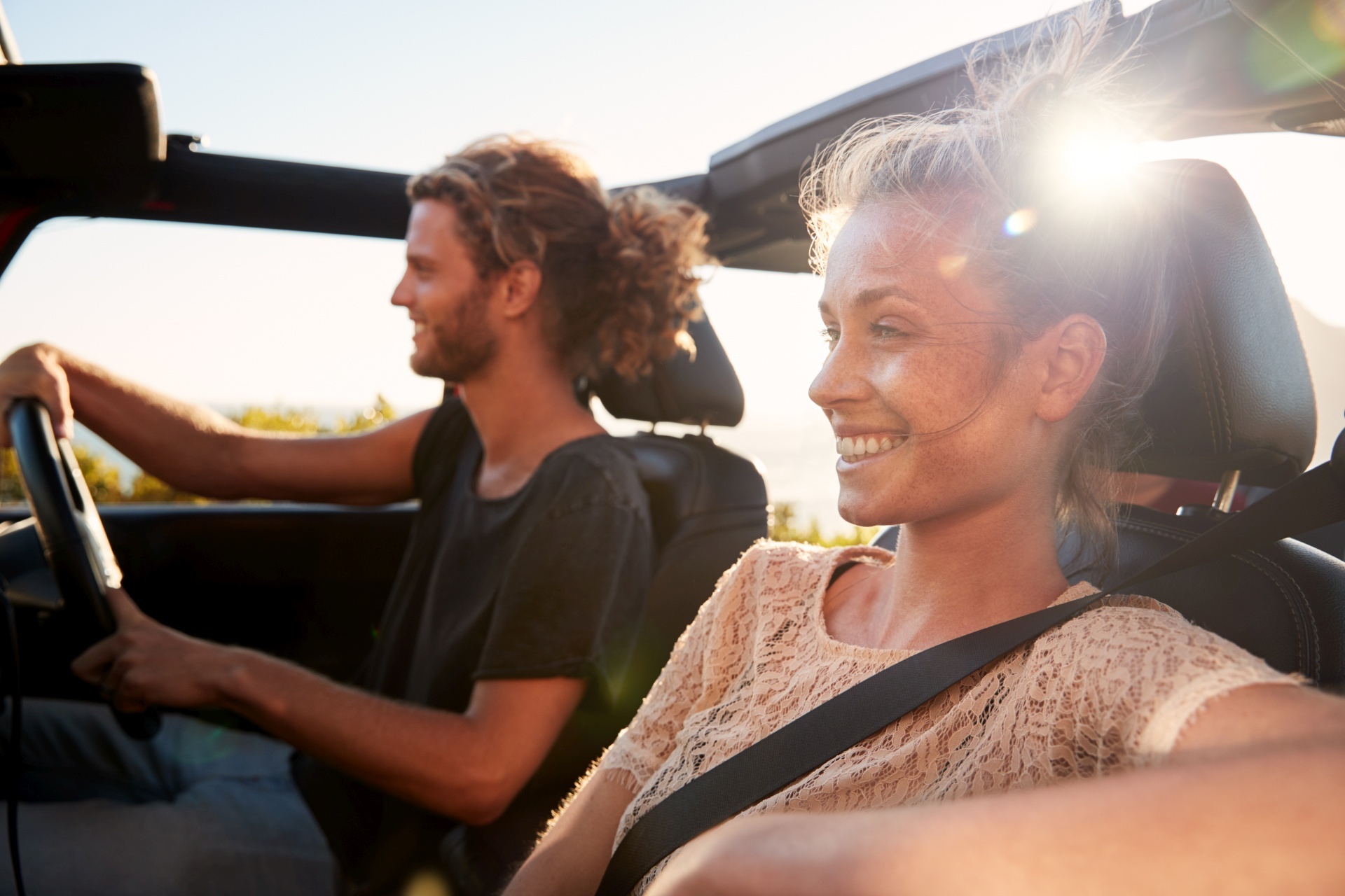 Millennial white couple on a road trip driving in an open top car, backlit, close up Millennial white couple on a road trip driving in an open top car, backlit, close up