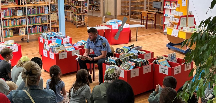 Ein Polizist sitzt auf einem Stuhl in einer Bücherei und liest Kindern Geschichten vor.