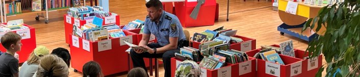 Ein Polizist sitzt auf einem Stuhl in einer Bücherei und liest Kindern Geschichten vor.