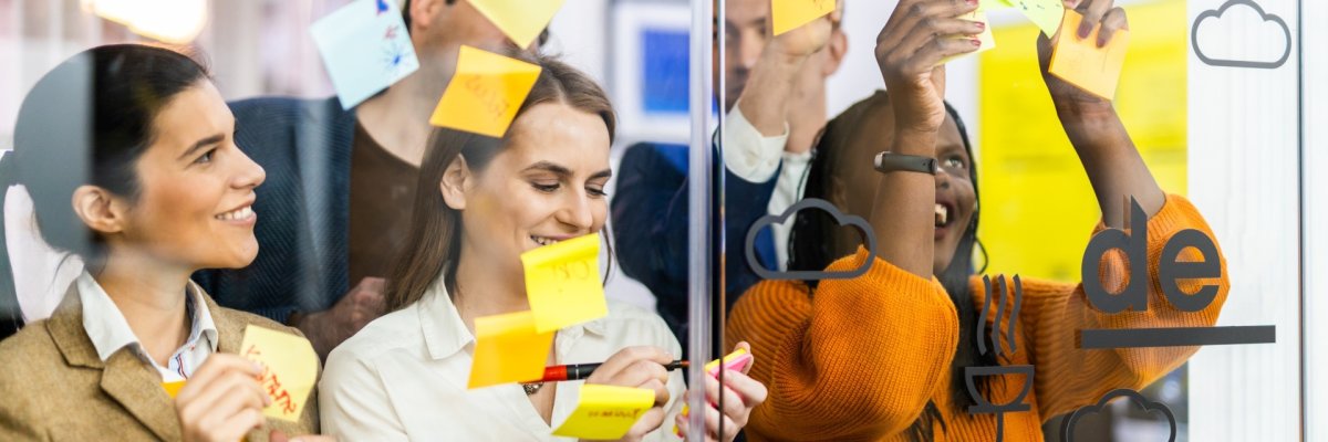 Menschen hängen in einem Büro Post-it-Zettel an eine Glasscheibe
